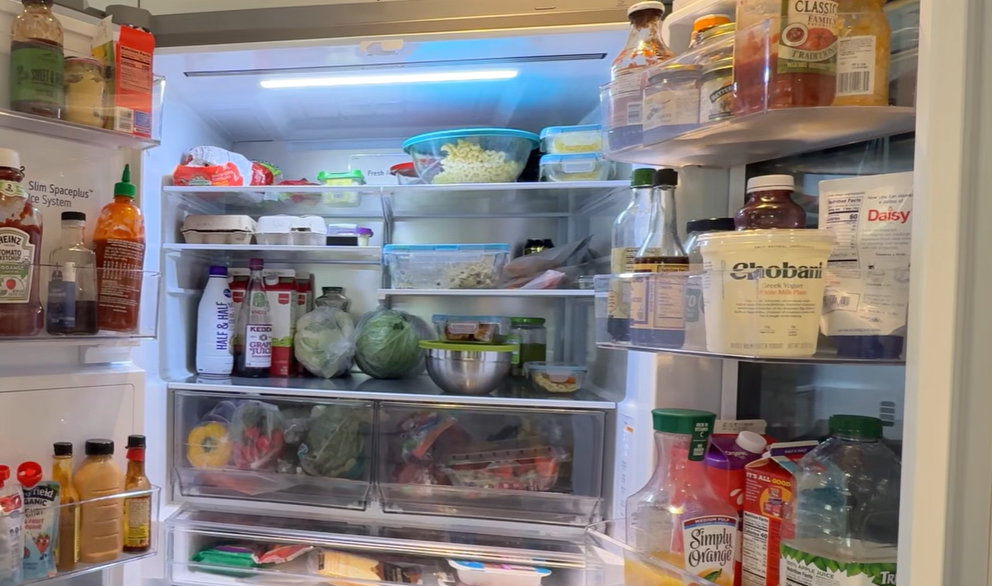 Open refrigerator with shelves, door bins and crisper drawers stocked with groceries